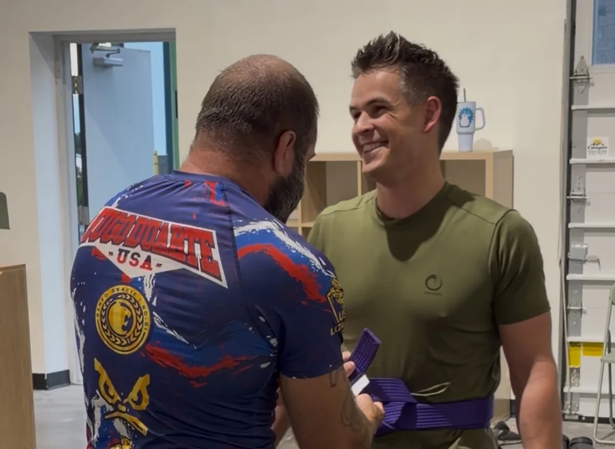 A Crossroads Combat Club member receiving a purple belt inside the gym.